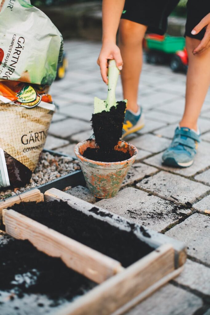 A child actively participates in gardening by shoveling soil into a pot on a patio.