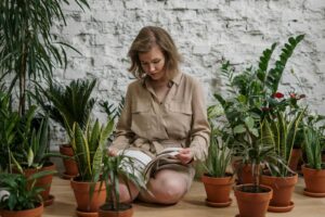 A woman sits among potted plants, enjoying a book in a cozy indoor setting.