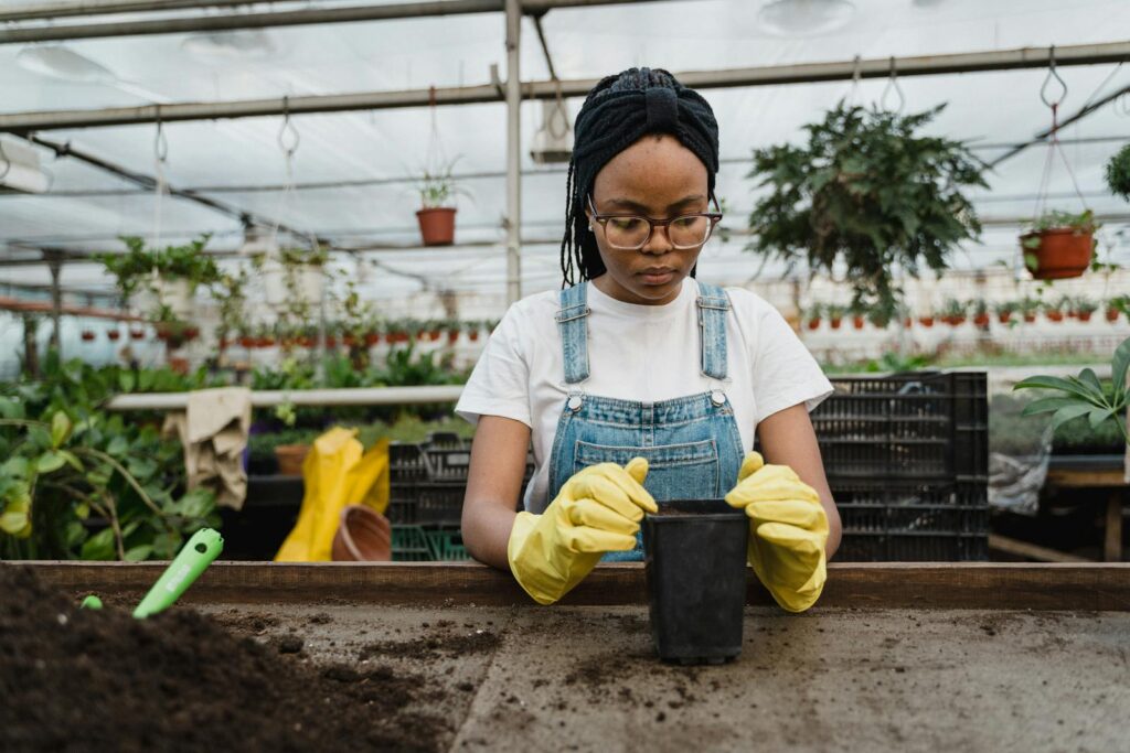 A dedicated woman gardening indoors wearing yellow gloves in a greenhouse.